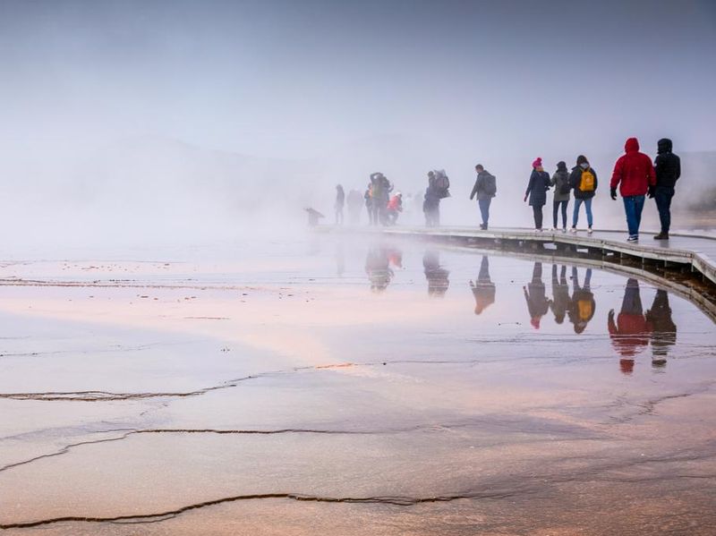 Misty scene of walking tourists on wooden boardwalk inside Grand Prismatic Spring.