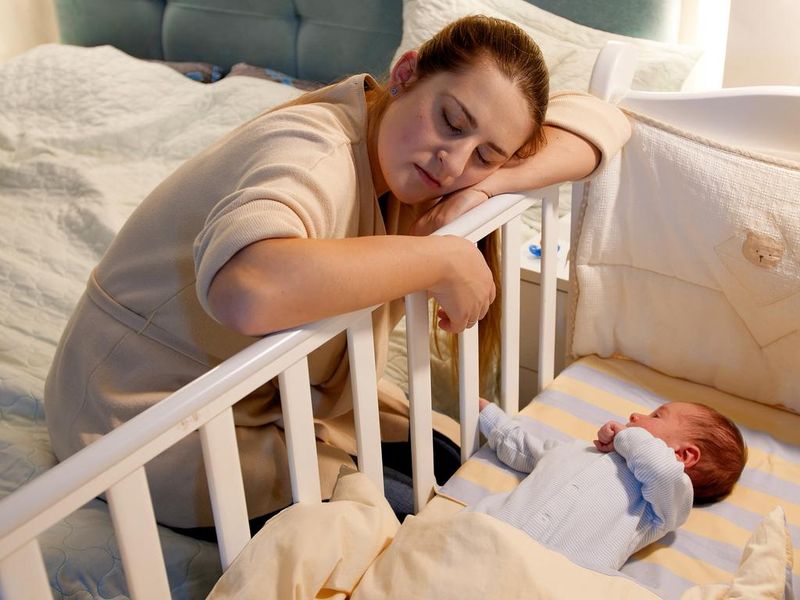 Mom falling asleep while rocking crib of her newborn baby