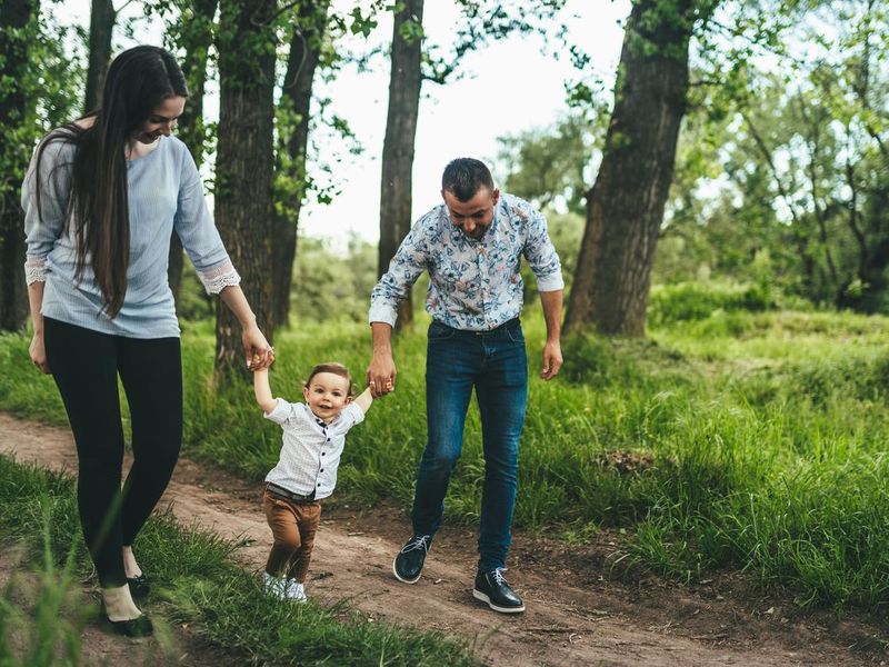Mother and father outdoors teaching baby boy to walk
