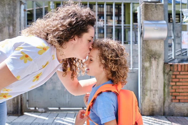 Mother kissing her son on the forehead at the entrance to a school