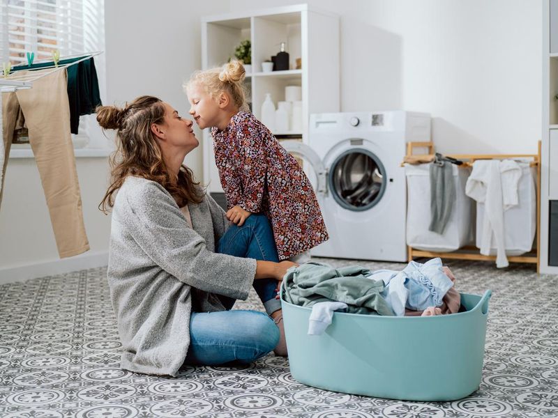 Mother sits on the laundry room floor with daughter cute little girl with blonde hair tied up in a bun wants to give the woman a kiss, parent's love for child