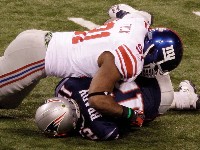 New York Giants defensive end Justin Tuck tackles New England Patriots quarterback Tom Brady