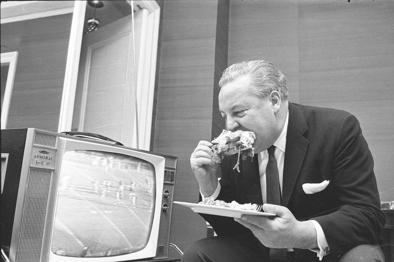New York Titans owner Harry Wismer eats turkey leg while watching football in 1962