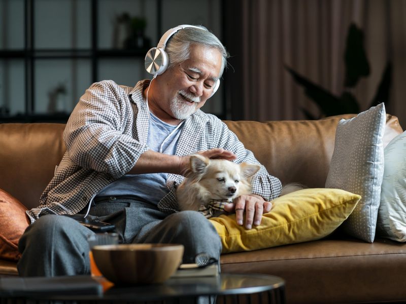 Older man wearing headphone relaxing on couch with Chihuahua dog