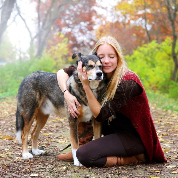 A happy, peaceful young woman has stopped walking her dog along a path in the autumn forest to hug him lovingly.