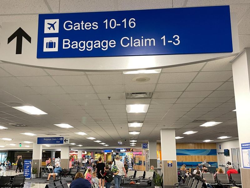 People waiting in the gate area to board a planes at the Sanford International Airport in Sanford, Florida with informational signs overhead pointing to gates and baggage claim.