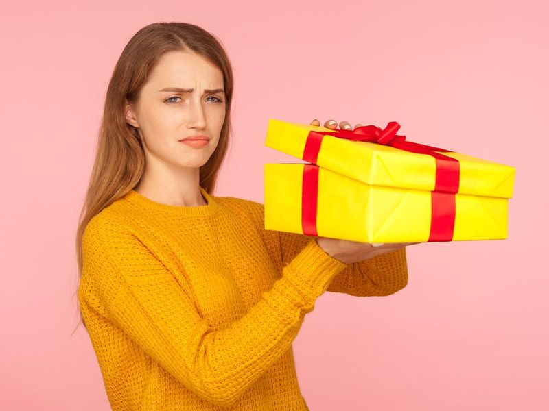 Portrait of unhappy red hair girl in sweater opening gift box and looking sadly at camera, disappointed with birthday surprise