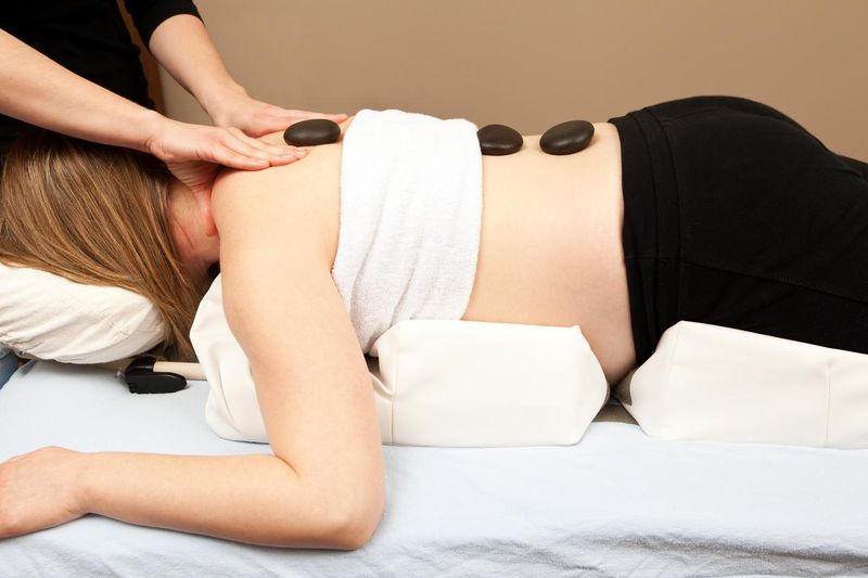 Pregnant woman getting prenatal massage with hot stones and bolster