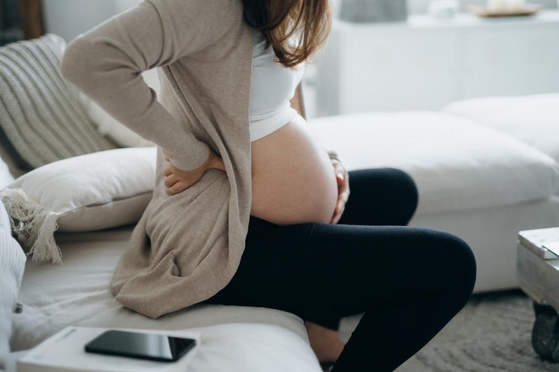 Pregnant woman touching her belly and lower back, suffering from backache. Pregnancy health, wellbeing concept