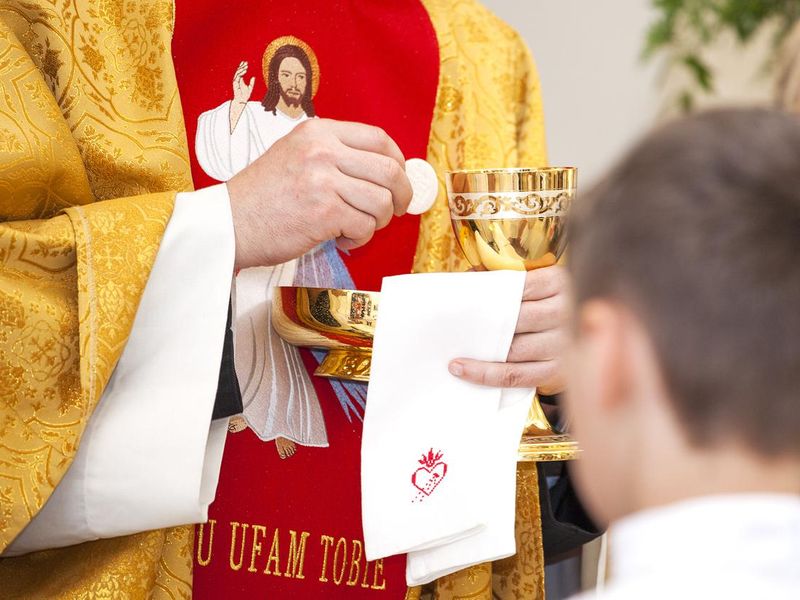 Priest gives first communion. Symbol of the body and blood of Christ.
