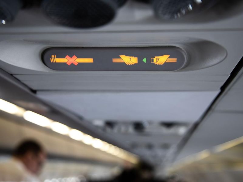 Prohibition signs in airplane shows crossed cigarette and recommendation to buckle up