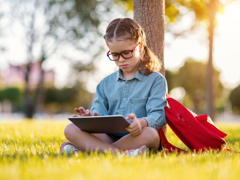 Schoolgirl reading a tablet in the park