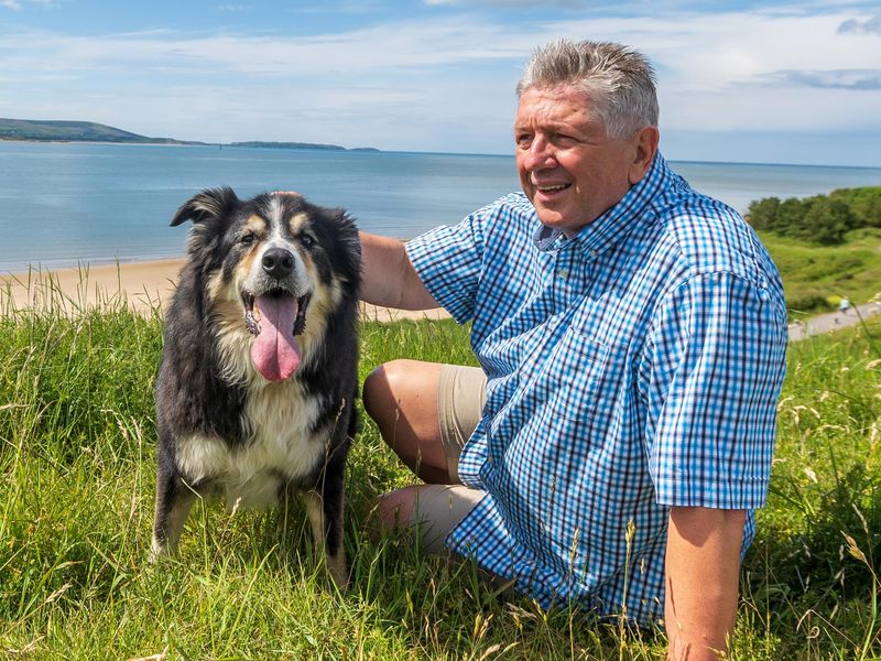 Senior man and dog resting on grass near a lake