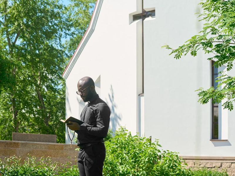 Side view of young preacher in black apparel looking in open Holy Bible