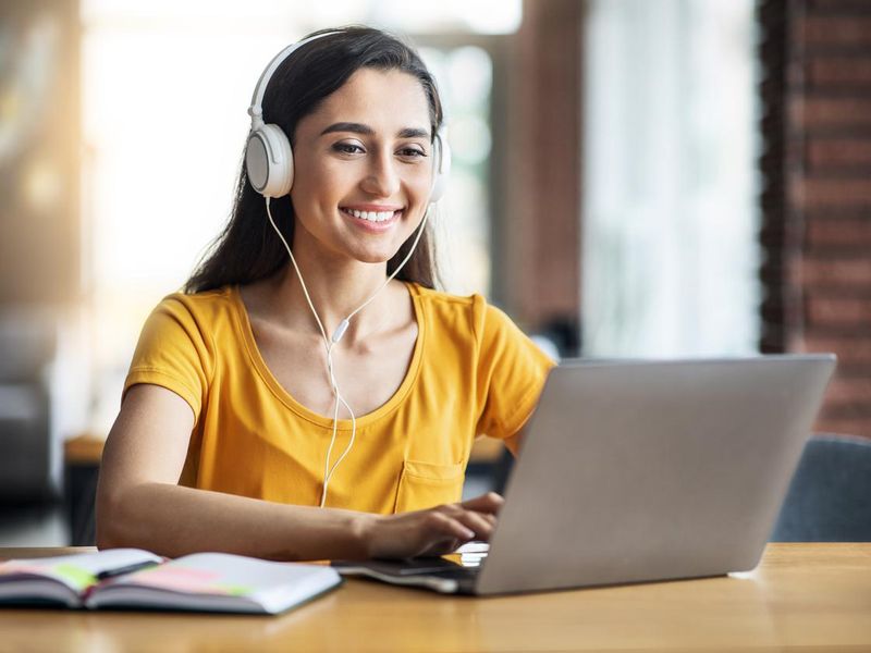 Smiling girl with headset studying online, using laptop