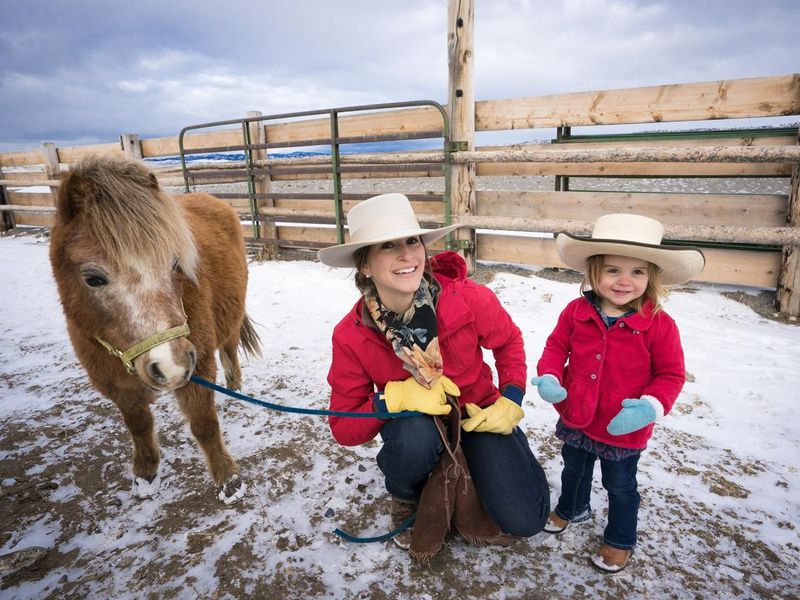 Smiling mother and 2 year old daughter on a ranch with a miniature horse
