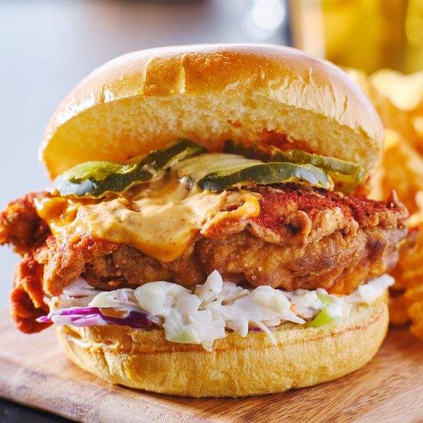 spicy nashville hot chicken sandwich with coleslaw and pickles on wooden cutting board