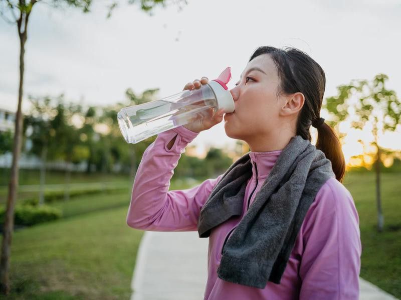 Sporty young Asian woman drinking water after jogging