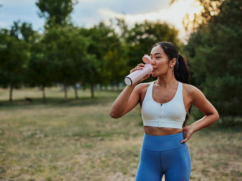 Sporty young woman drinking water while exercising at the park