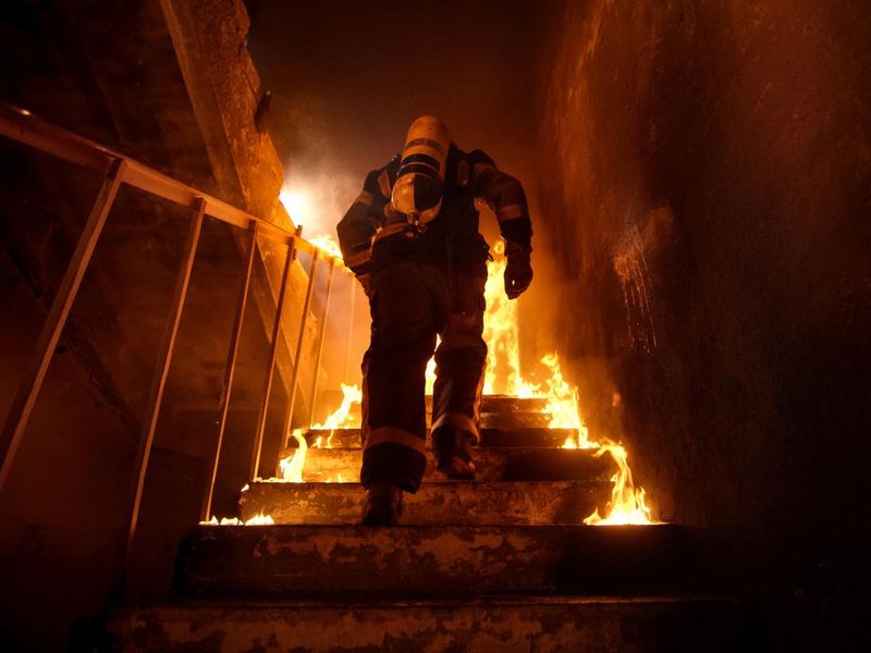 Strong and brave Firefighter going up stairs in burning building