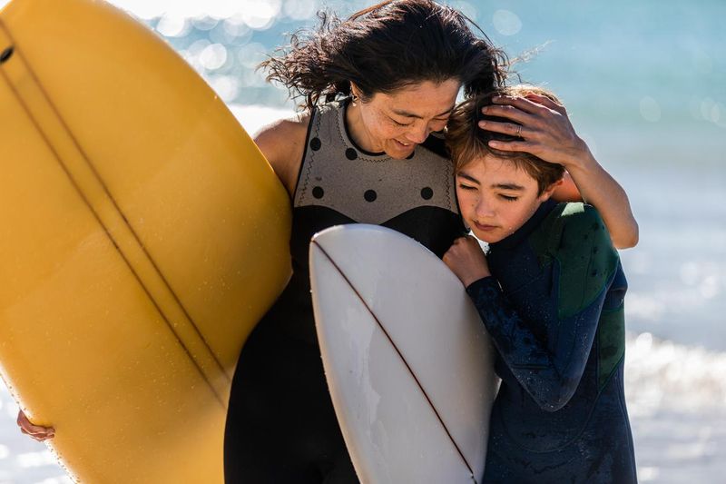 Surfing mum and son cuddle up as they leave the water together