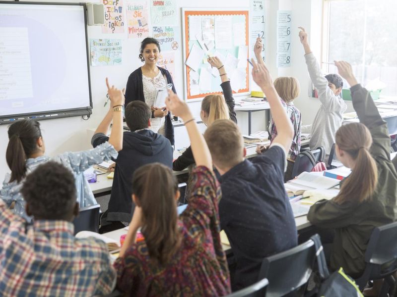 Teacher with teenage students raising hands in classroom