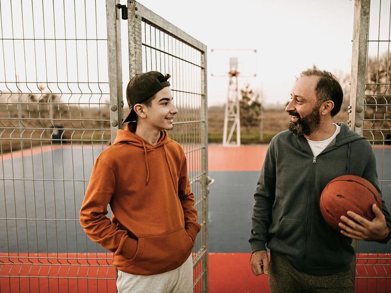 Teenager boy and father standing at front of the basketball court