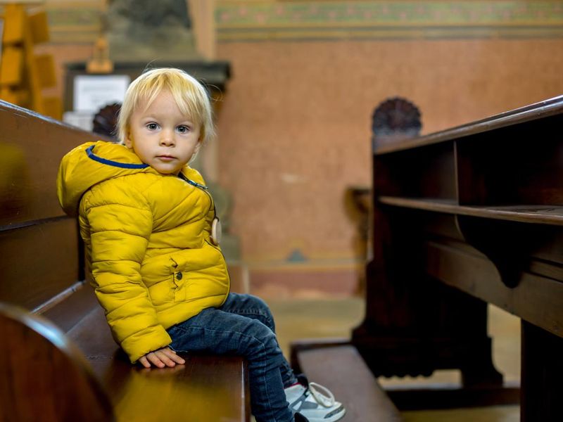 Toddler child sitting on a praying bench in church