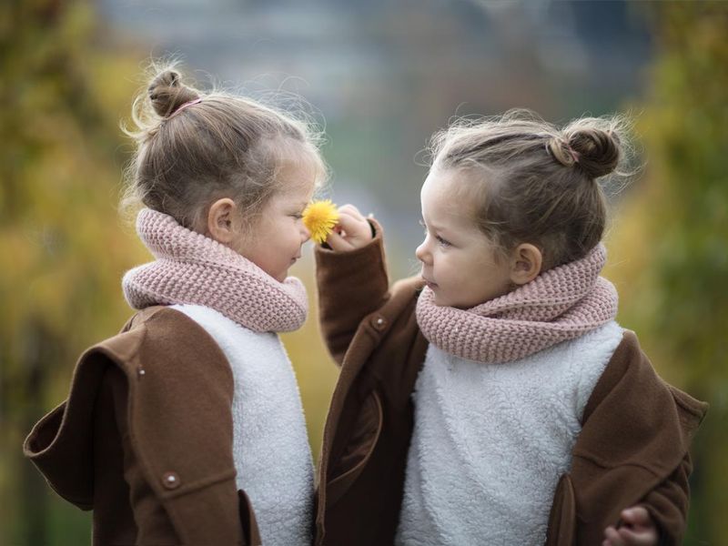 Two identical twin girls smelling a flower