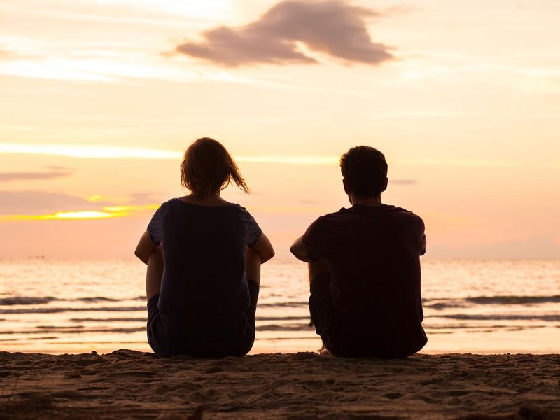 two people sitting together on the beach