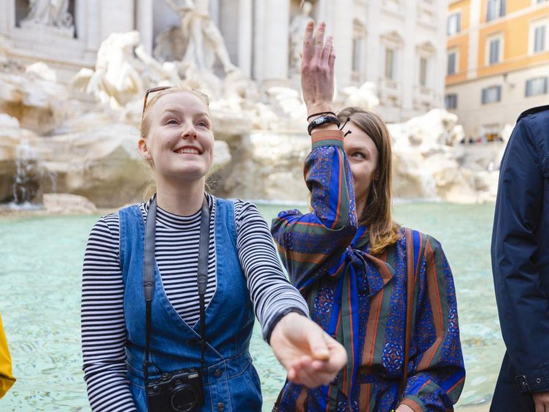 Two women sitting on the Trevi Fountain wall in Rome, Italy