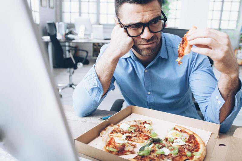 Unhappy businessman eating pizza at work