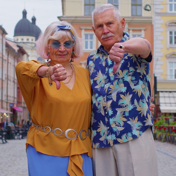 Upset senior old stylish tourists man and woman showing thumbs down sign gesture, expressing discontent, disapproval, dissatisfied, dislike. Elderly grandmother, grandfather family traveling together