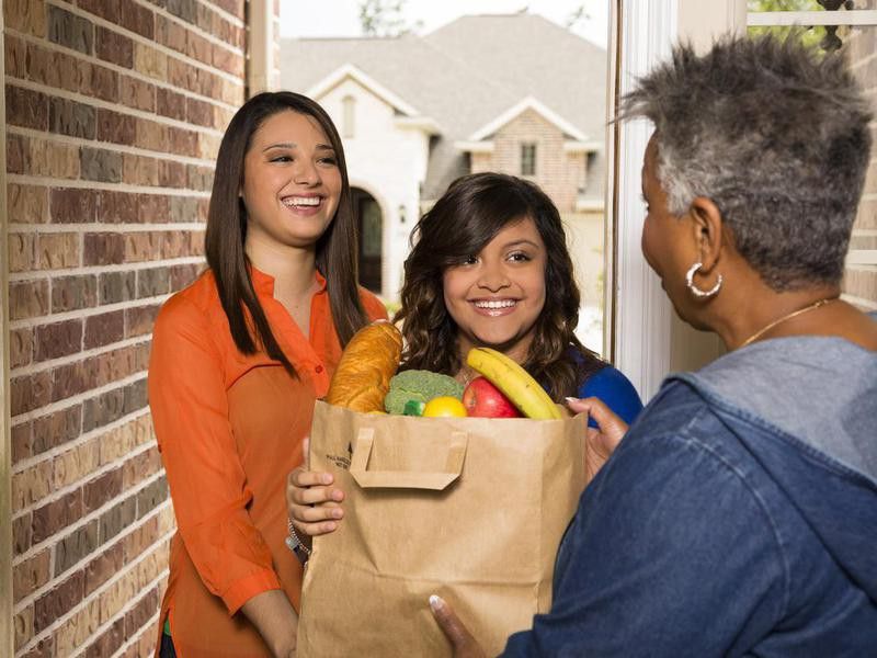 Volunteers:  Young adults bring groceries to senior woman.