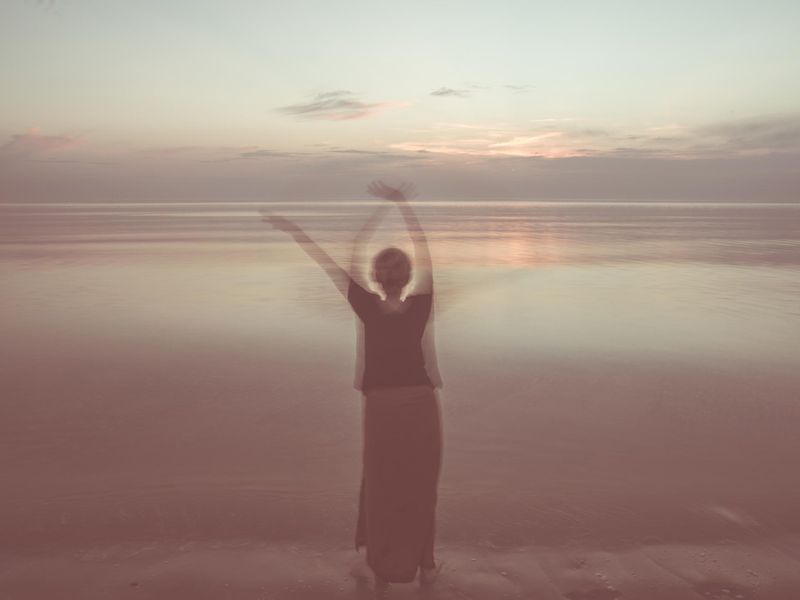 woman dancing and waving by the sea at sundown
