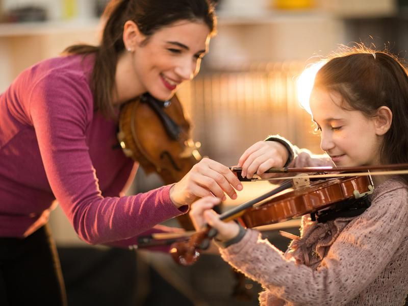Woman giving violin lesson to kid