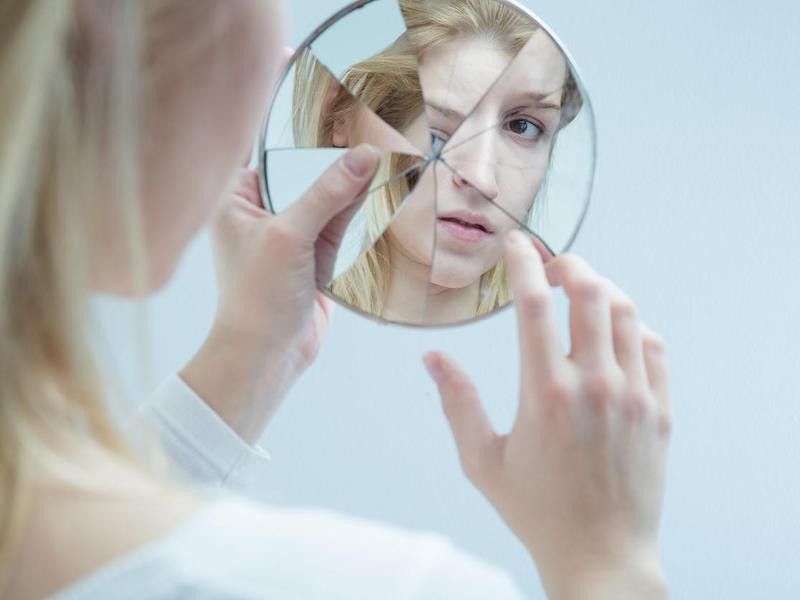 Woman looking into broken mirror