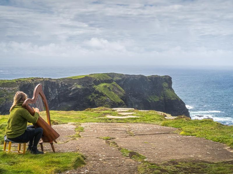 Woman playing harp on the top of iconic Cliffs of Moher, Ireland
