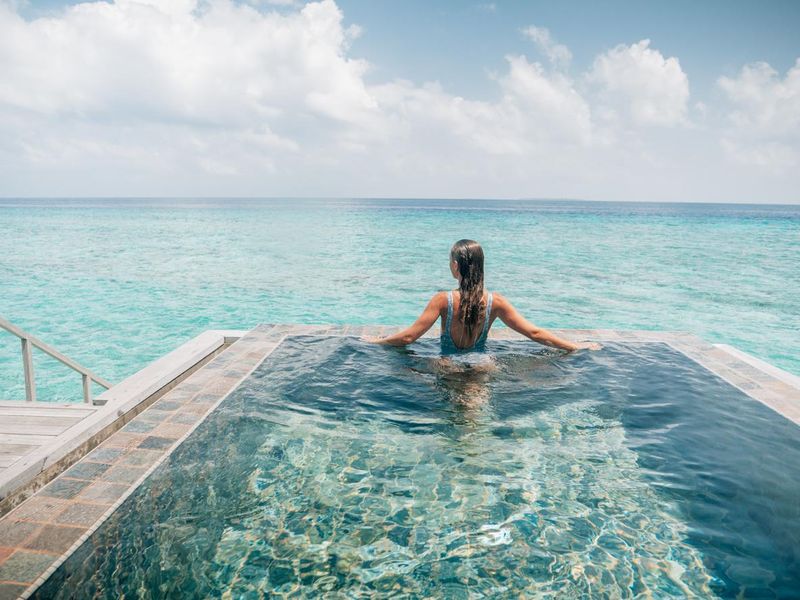 Woman relaxes inside infinity pool over reef lagoon