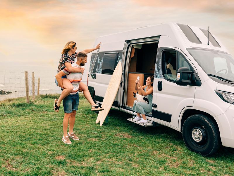 Woman taking photo of friends next to camper van during road trip
