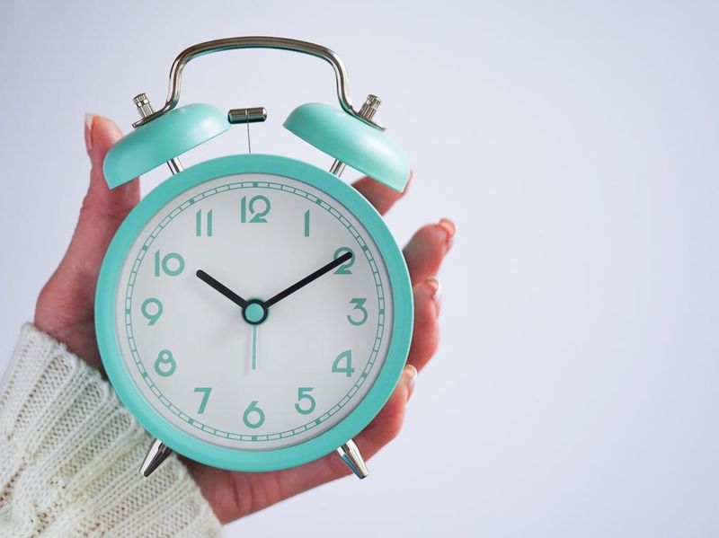 Woman's hand holding blue retro alarm clock