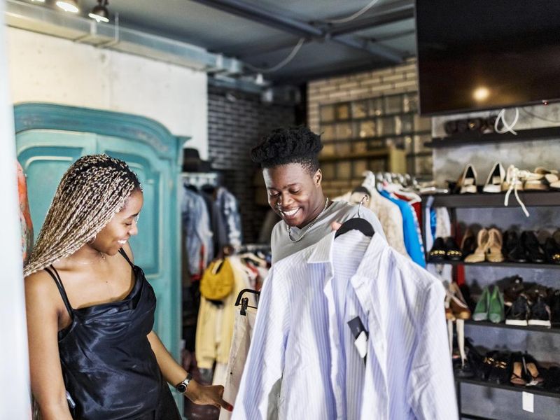 Young adult African couple choosing dress at second hand sale stock