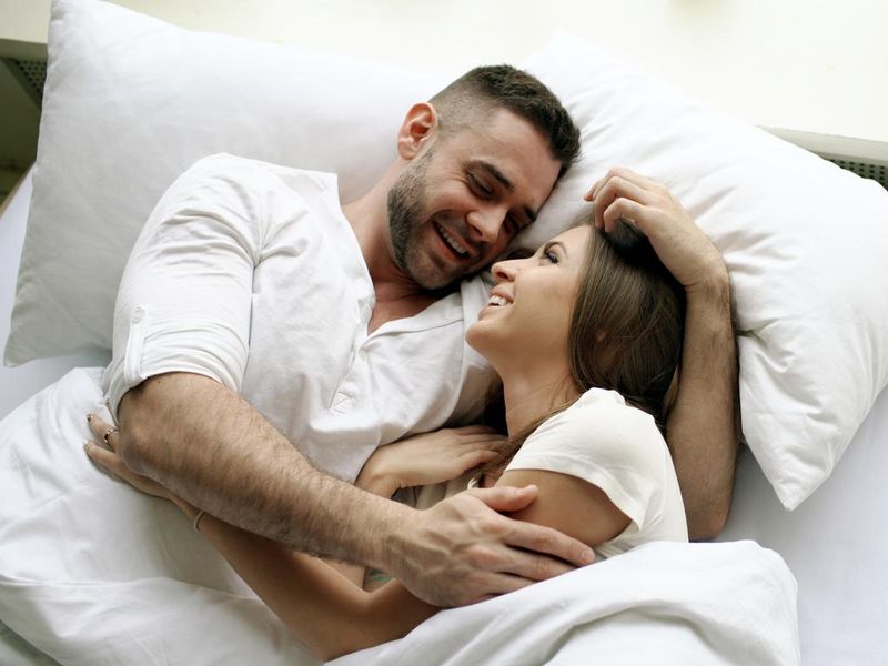 Young beautiful and loving couple talk and hug in bed