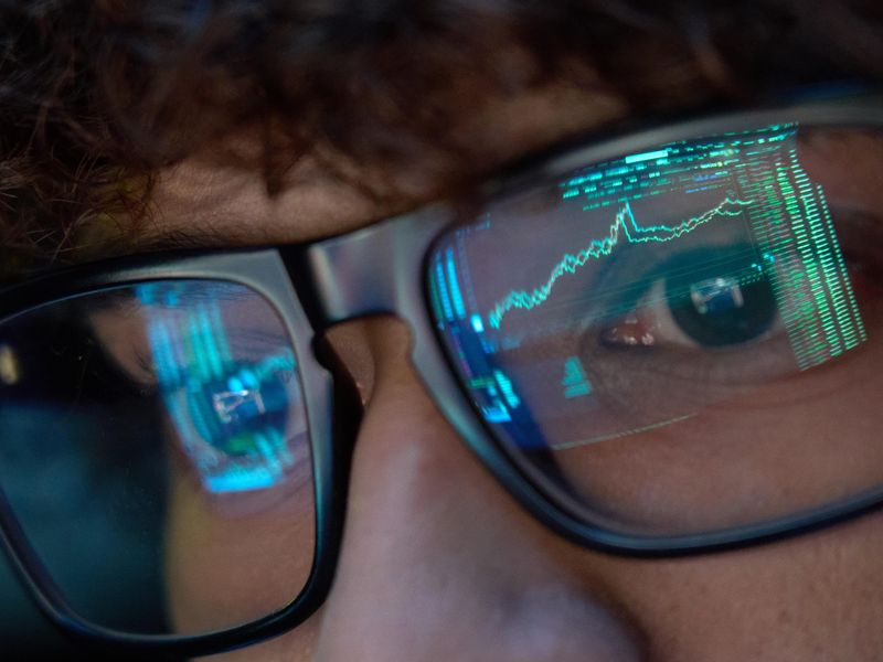 Young businessman looking at trading charts reflecting in his glasses