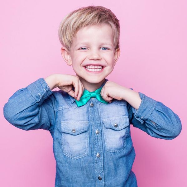 Young beautiful boy with blue shirt and butterfly tie. Studio portrait over pink background