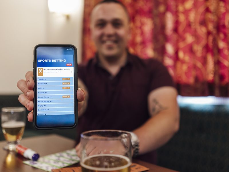 Young man in social club showing a sports betting app on his phone