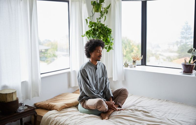 Young man meditating on bed