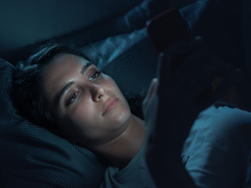 Young woman can't sleep while lying in bed with her smartphone