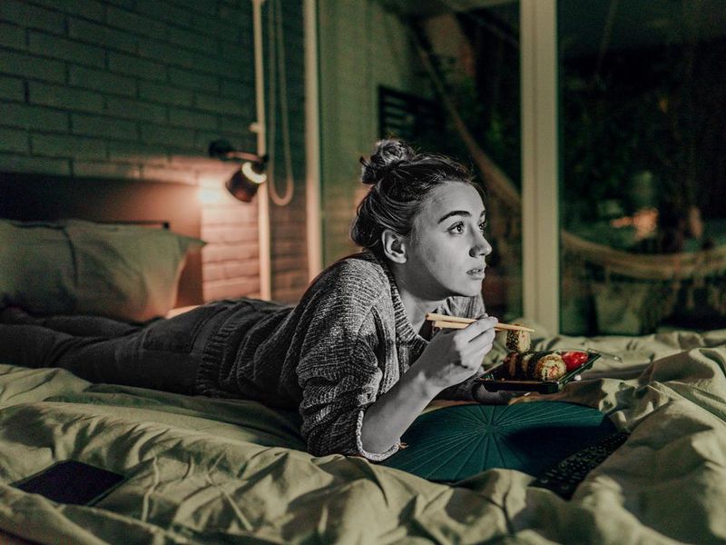 Young woman eating sushi in bed
