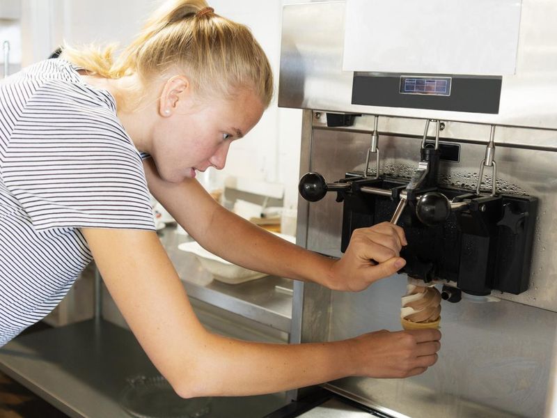 Young woman making a soft serve ice cream from a machine